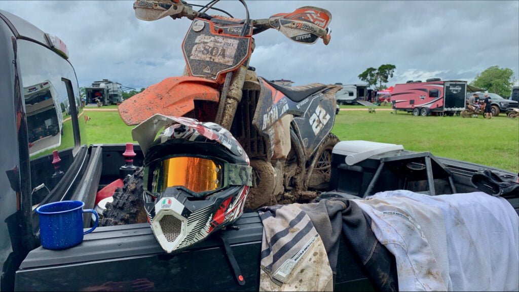 Dirty dirt bike and a helmet plus other gear on a truck bed after an enduro dirt bike race