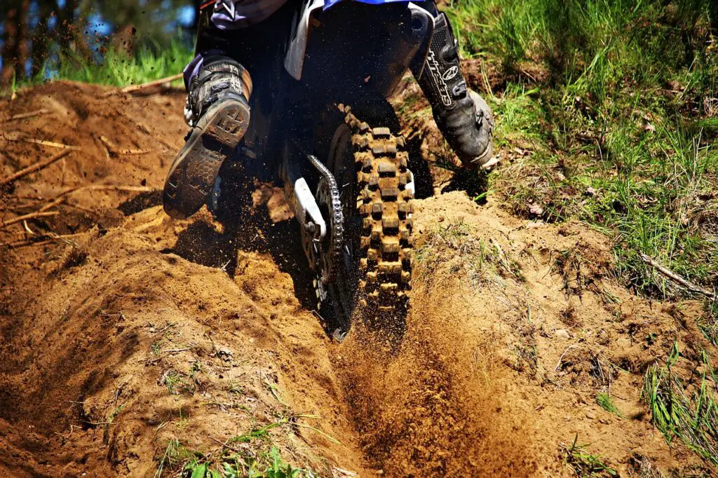 Enduro dirt bike climbing a sandy hill with rear tire in a berm and blasting sand