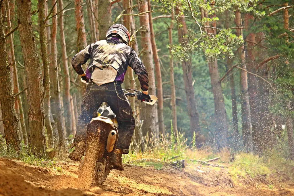 Man riding on an enduro dirt bike and blasting sand in the woods with a good dirt bike setup for beginners