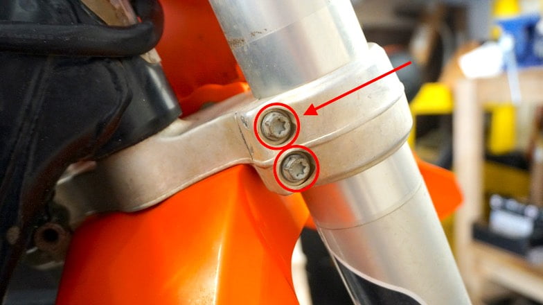 Bottom of the triple tree of a dirt bike with two right fork leg bolts circled in red