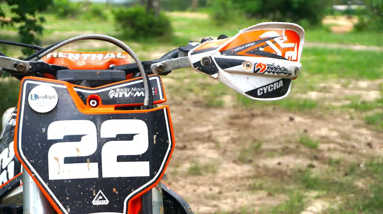 Dirt bike handlebars with a handguard and number plate in front of the bike
