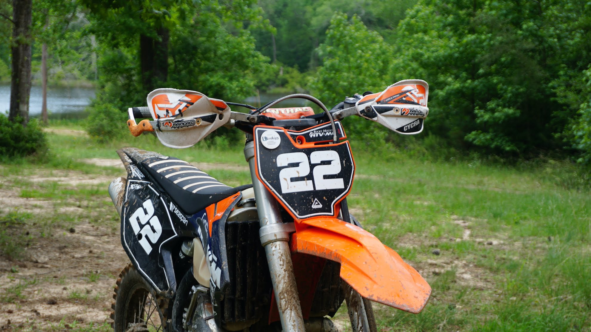 Front side of a muddy dirt bike and handlebars with handguards and a number plate
