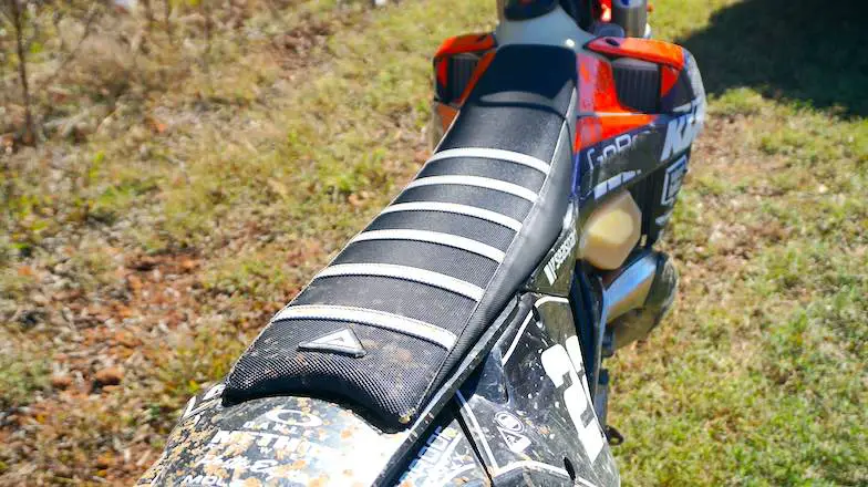 A close-up of a muddy dirt bike seat with white ribs
