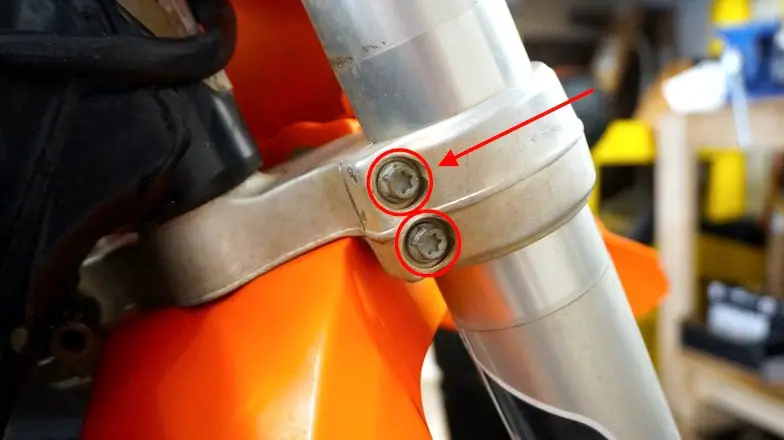 Bottom of the triple tree of a dirt bike with two bolts circled in red