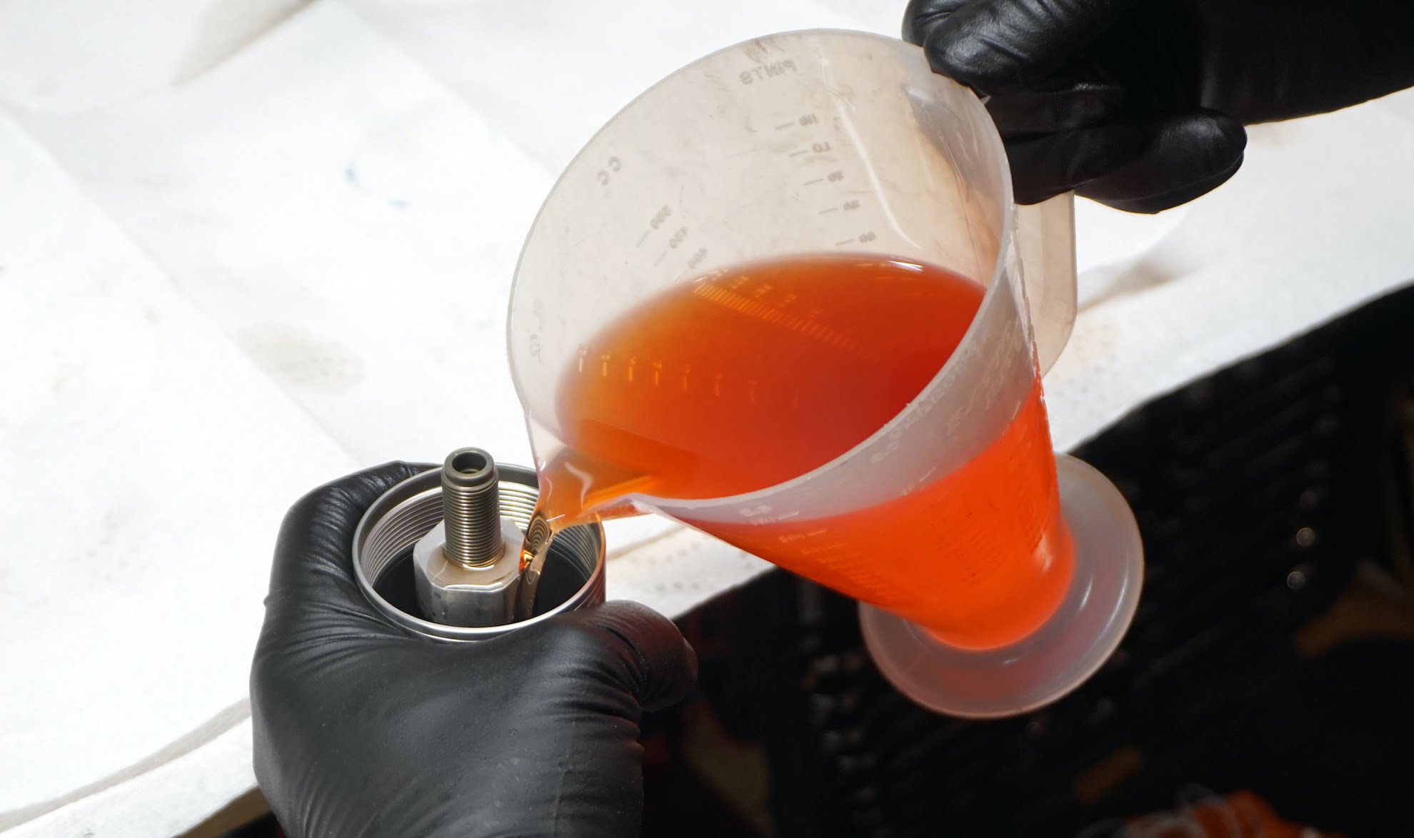 A hand holding a measuring cup filled with fresh fork oil and pouring it inside the front fork