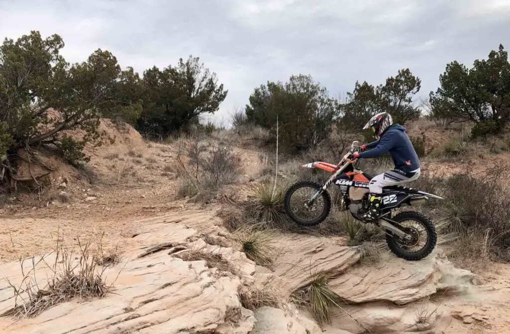 Man riding a dirt bike over a ledge with front wheel in the air