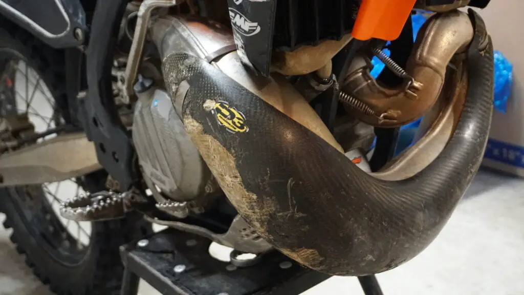 Old carbon fiber pipe guard with wear and tear on a 2-stroke dirt bike