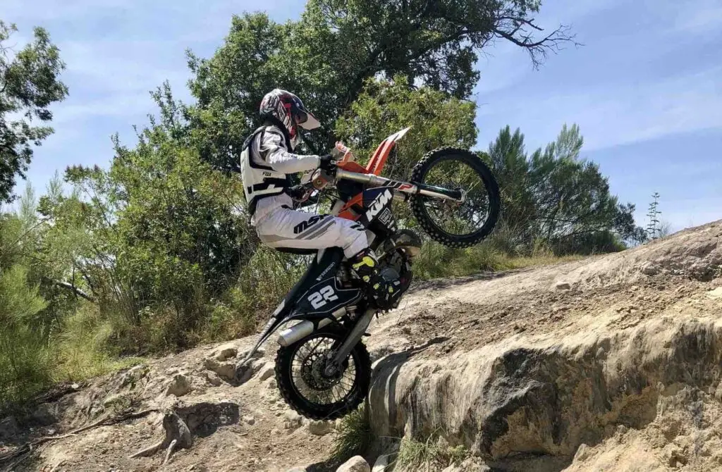 Man jumping over a rocky ledge on a dirt bike with front wheel up in the air