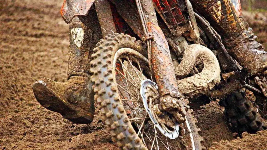 Dirt bike on a muddy track with the lower part of the dirt bike and riding boots covered in mud