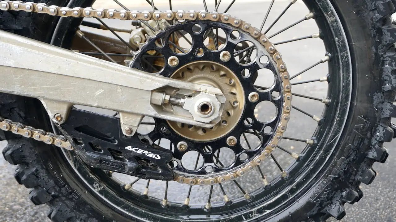 A black dirt bike chain guide block installed in front of the rear sprocket