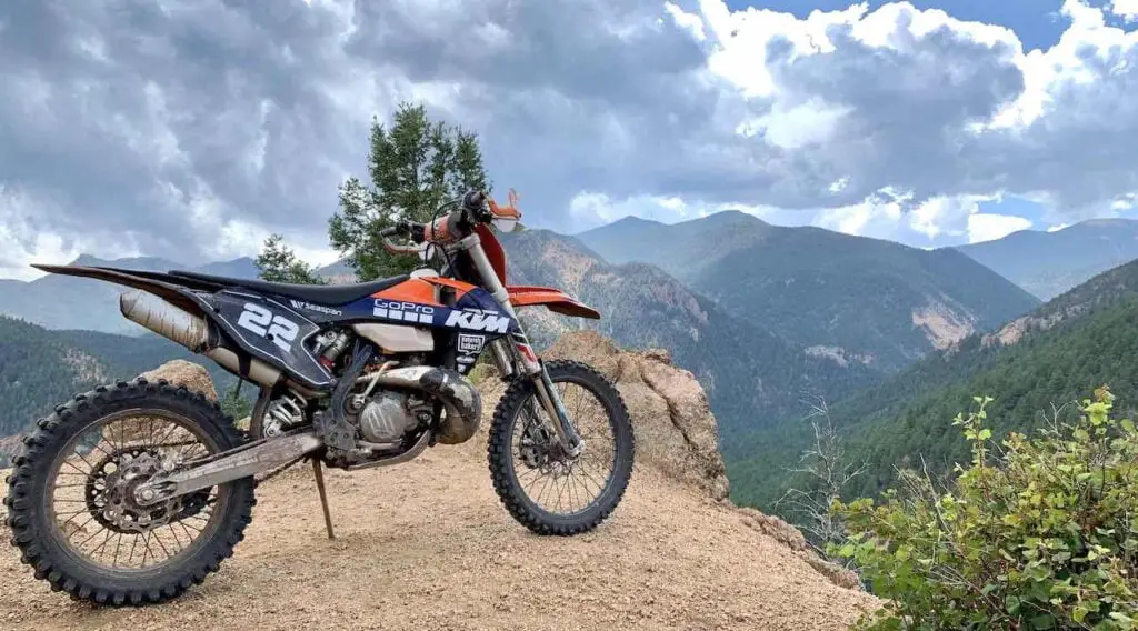 KTM dirt bike standing on a cliff with mountains in the background