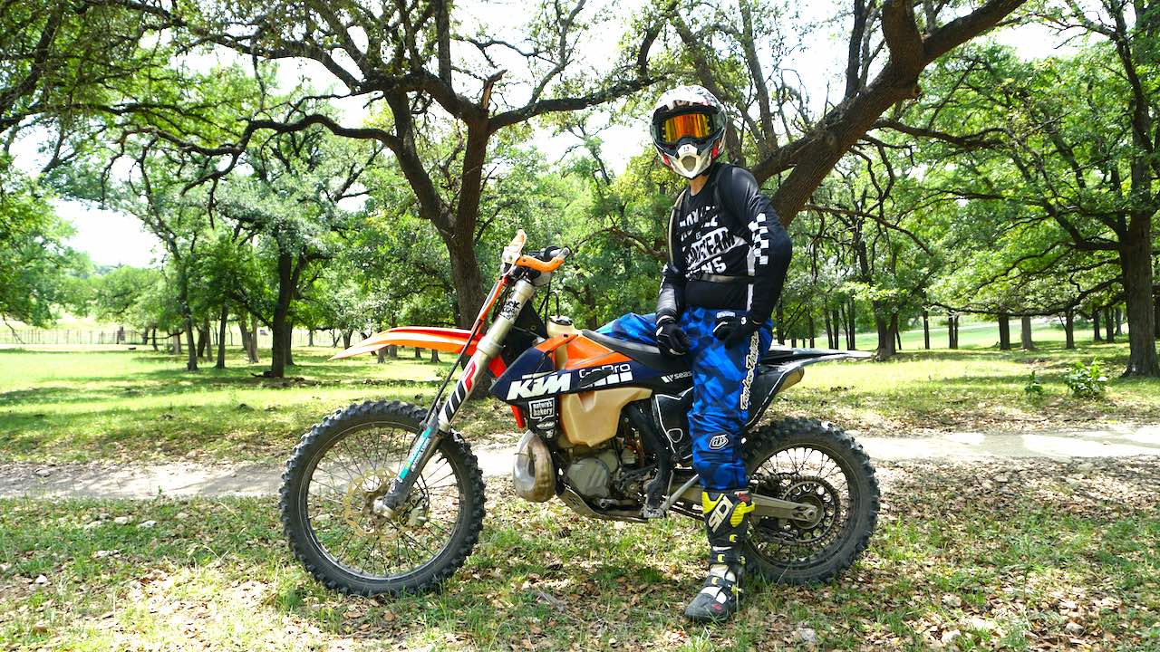 Dirt bike rider wearing full riding gear and sitting on a KTM with lush trees on the background