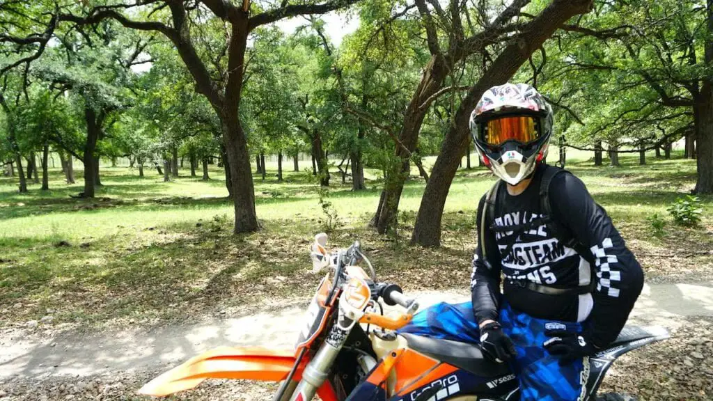 Dirt bike rider wearing full riding gear and sitting on a KTM with lush trees on the background
