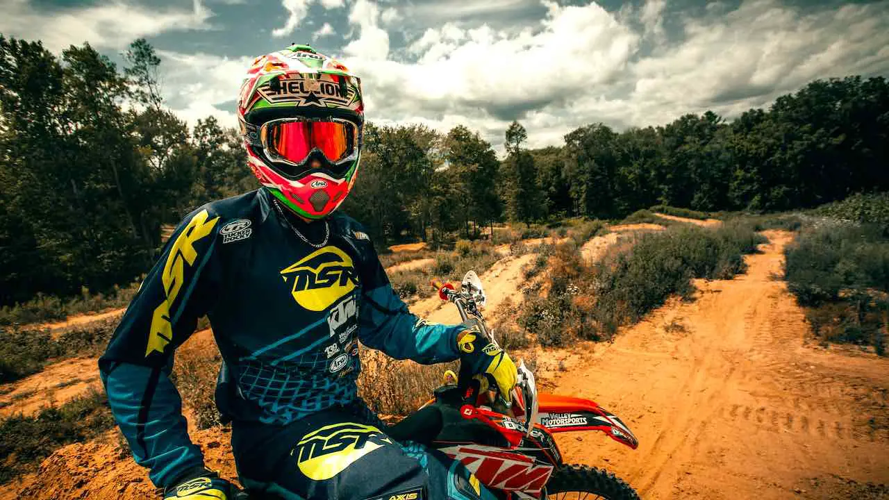 A rider wearing dirt bike gear for hot weather and sitting on a dirt bike with sandy trails on the background