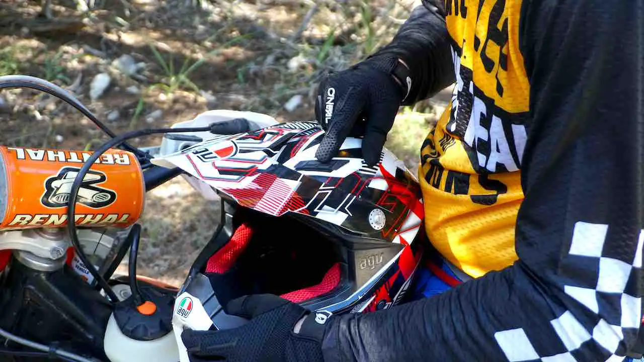 A dirt bike helmet on the rider's lap with a finger pointing at an air vent modified for hot weather riding