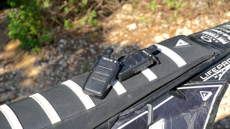 Retevis RT19 dirt bike radios laying on a dirt bike seat with a single trail on the background