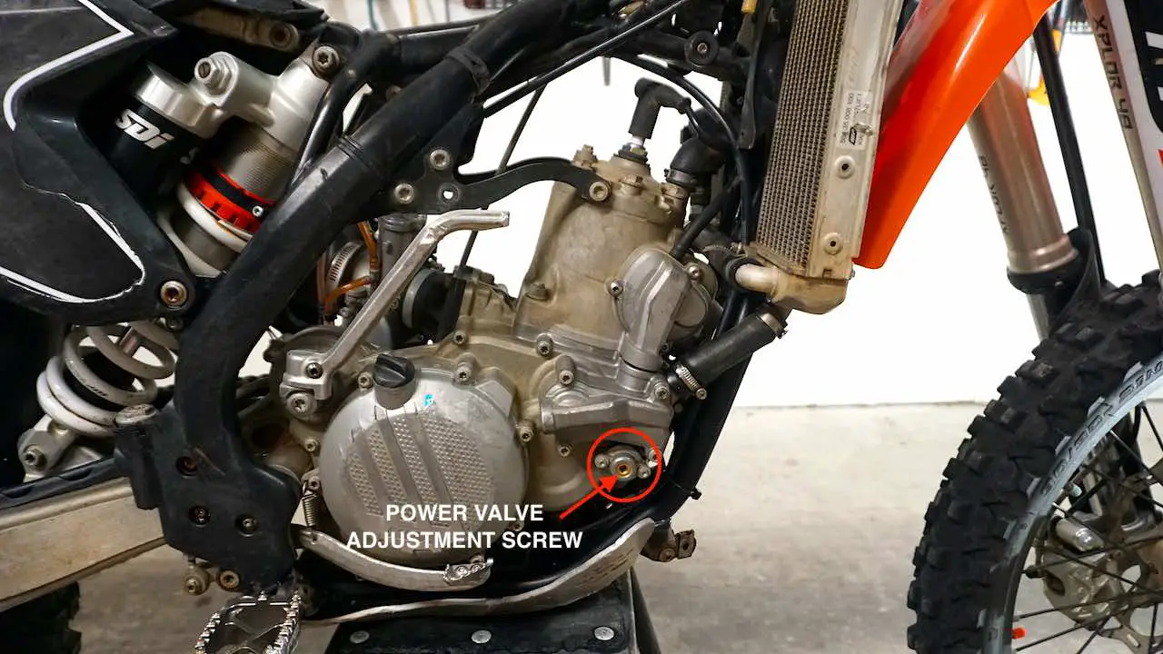 A dirt bike motor with a red circle around the power valve adjustment screw and a red arrow pointing at it