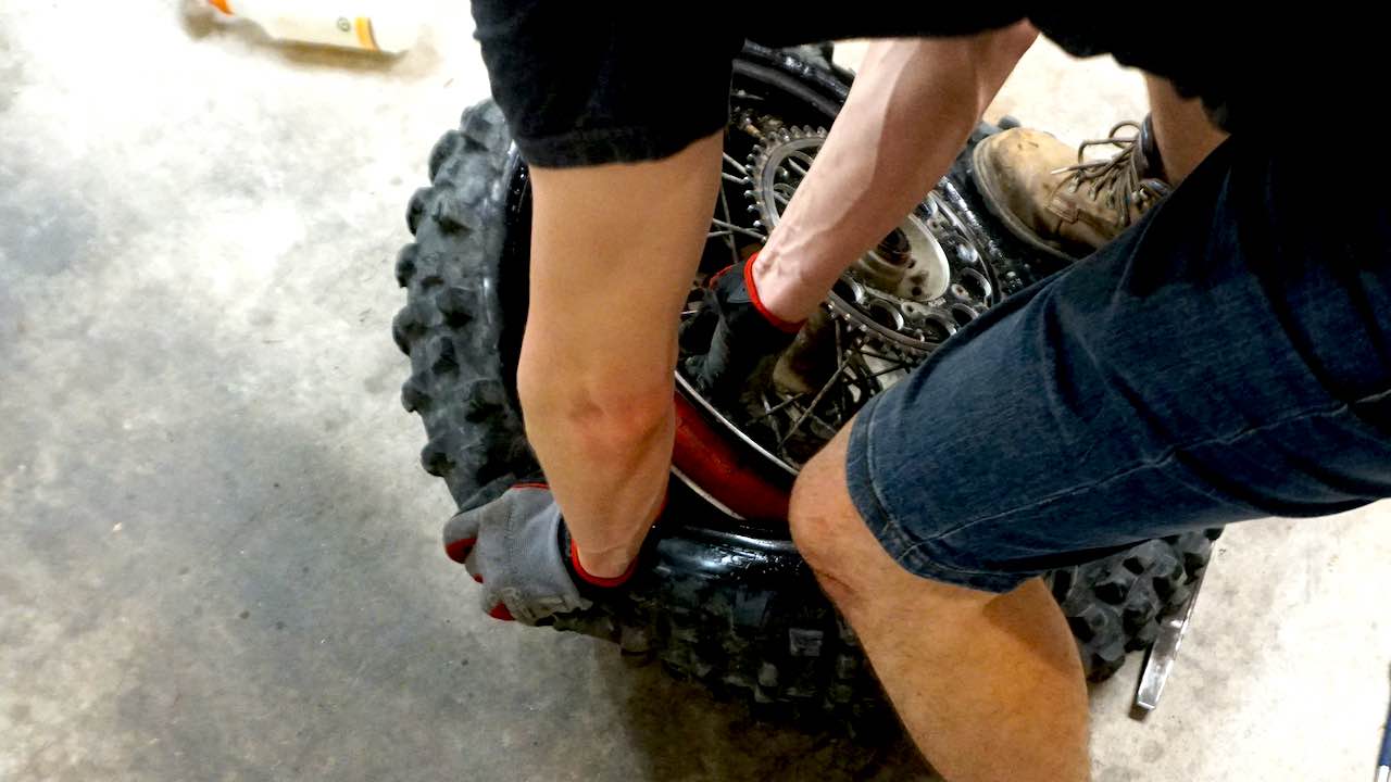 Hands pulling a wheel off an old dirt bike tire while changing the tire