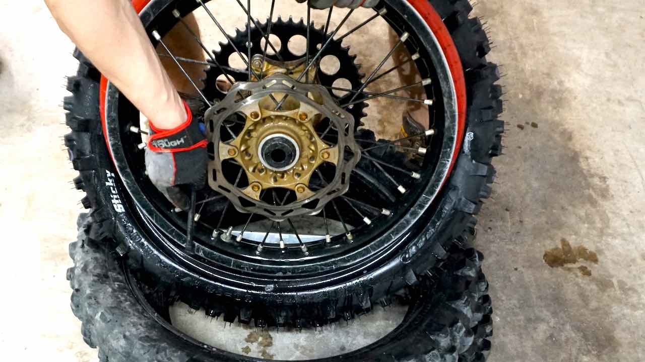 A hand pushing a wheel inside a new dirt bike tire with a rim lock