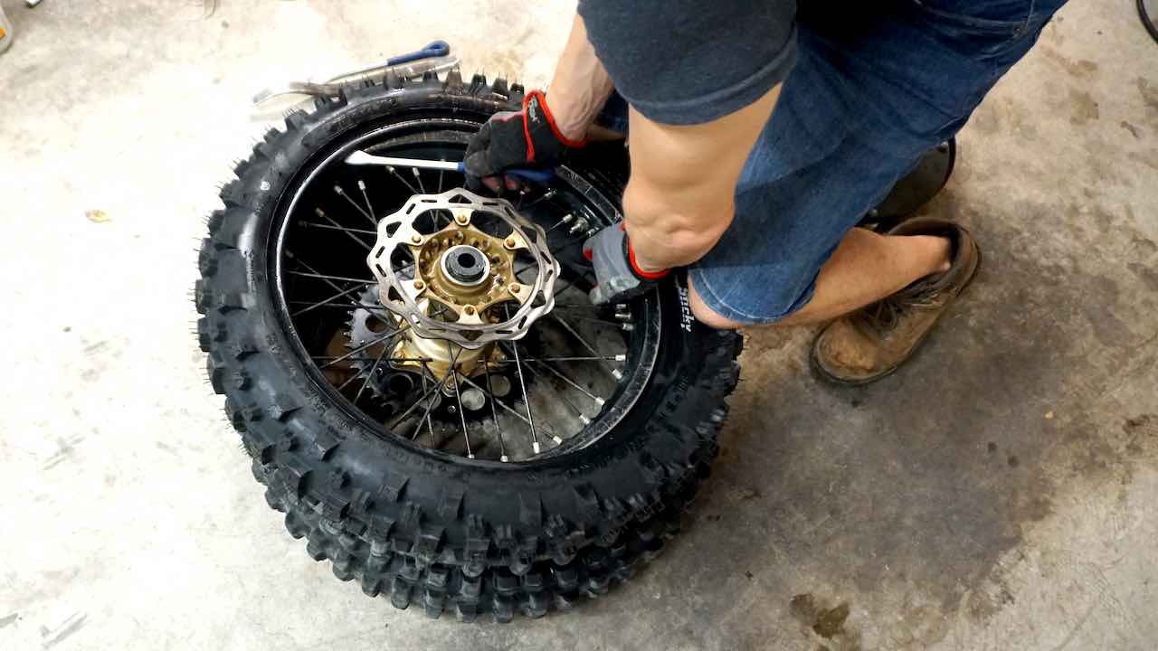 A man installing a tire bead onto a wheel with tire spoons while pushing the tire down with knees