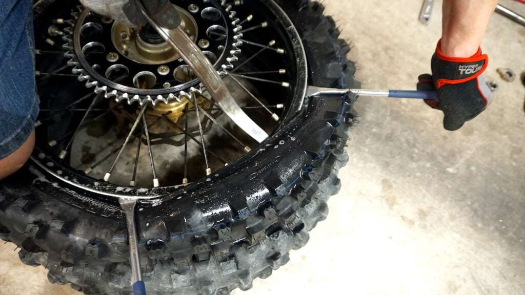 Hands holding tire spoons to push the tire bead on the wheel while changing a dirt bike tire