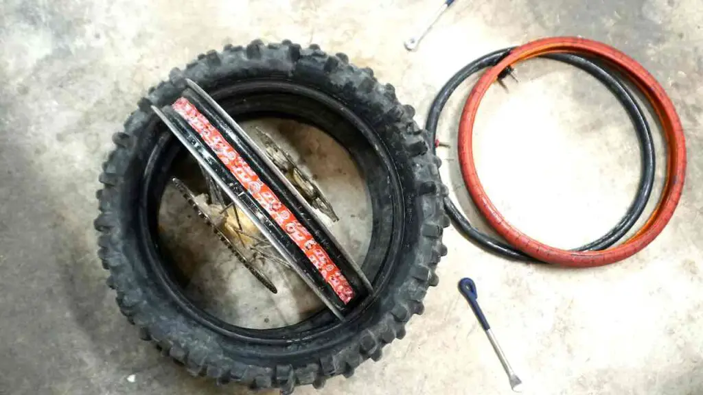 A red Tubliss tube, a black inner tube and tire spoons laying on a ground next to the wheel and an old tire