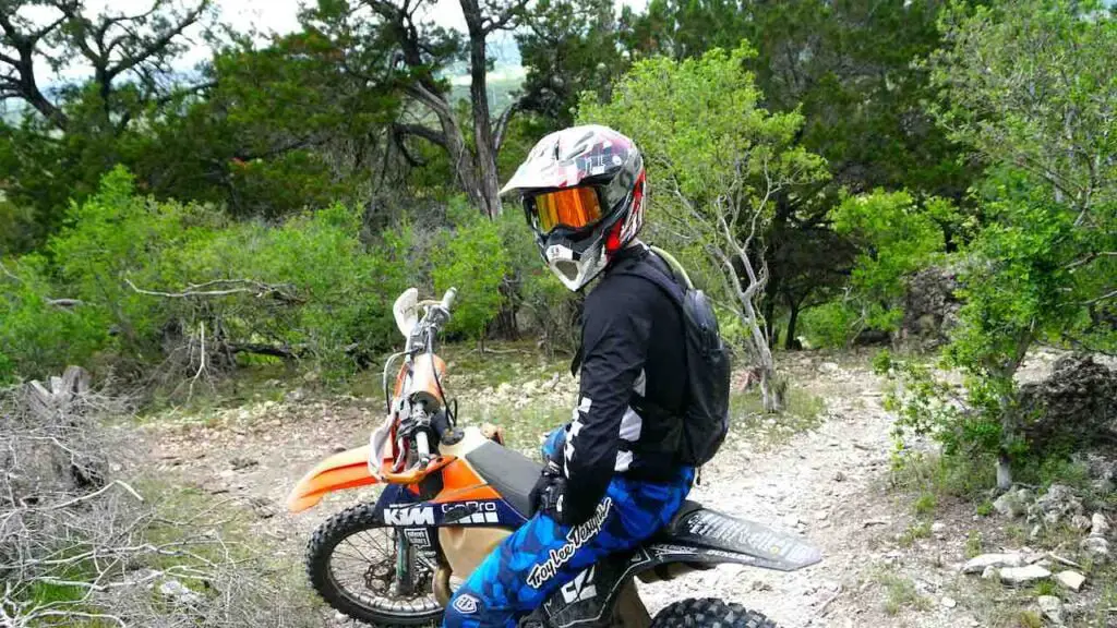Dirt bike rider sitting on a bike wearing full gear and a dirt bike backpack with trees on the background