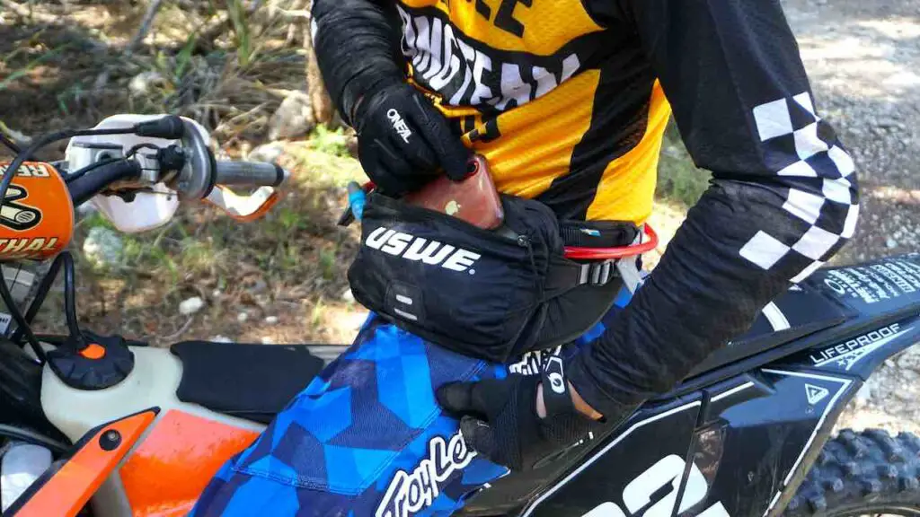 A dirt bike rider opening a fanny pack and showing phone and compartments inside