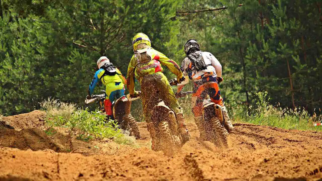 Three dirt bike riders riding in a stand-up position on a single track in a forest