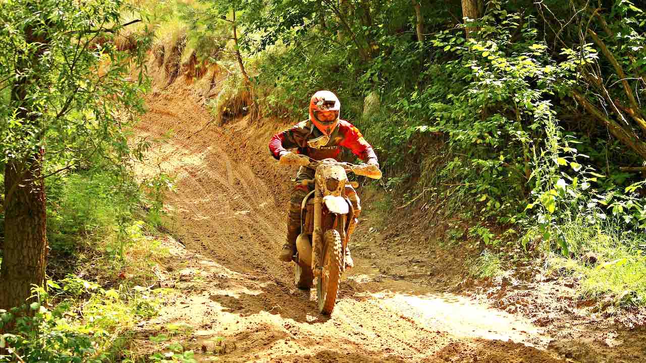 A man in full riding gear riding a dirt bike on a single track lined with trees