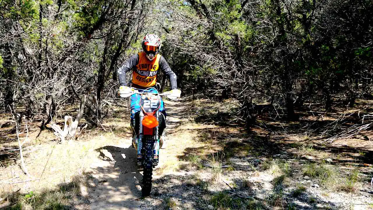 Dirt bike rider standing on the pegs while riding on a single track in the forest