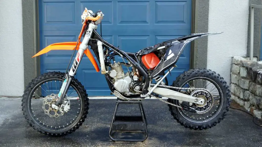 A washed dirt bike standing on a center stand with the seat, upper plastics, gas tank, and exhaust pipe removed