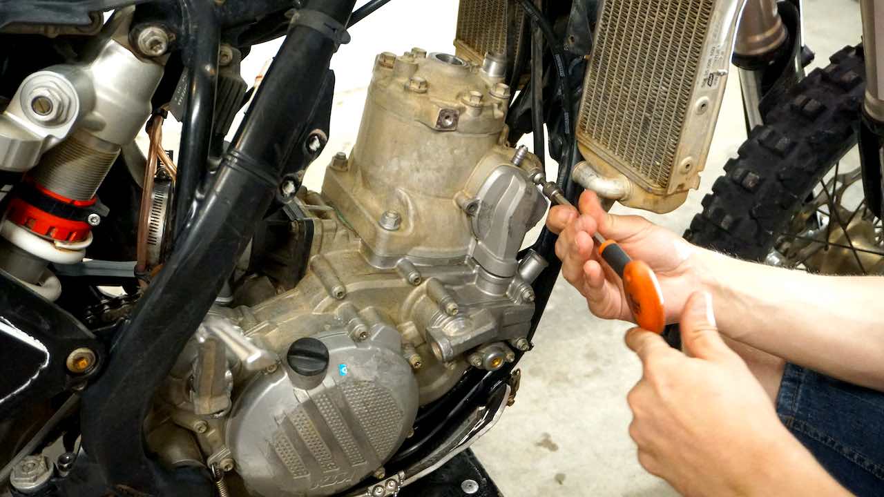 Hands holding a T-handle tool and removing a power valve cover bolt
