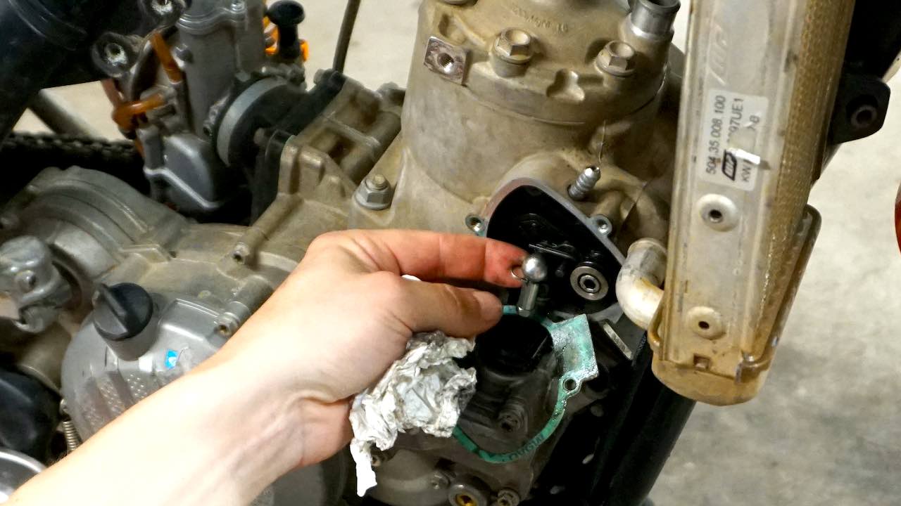A hand removing a circlip from the power valve push rod while performing a 2 stroke top end rebuild