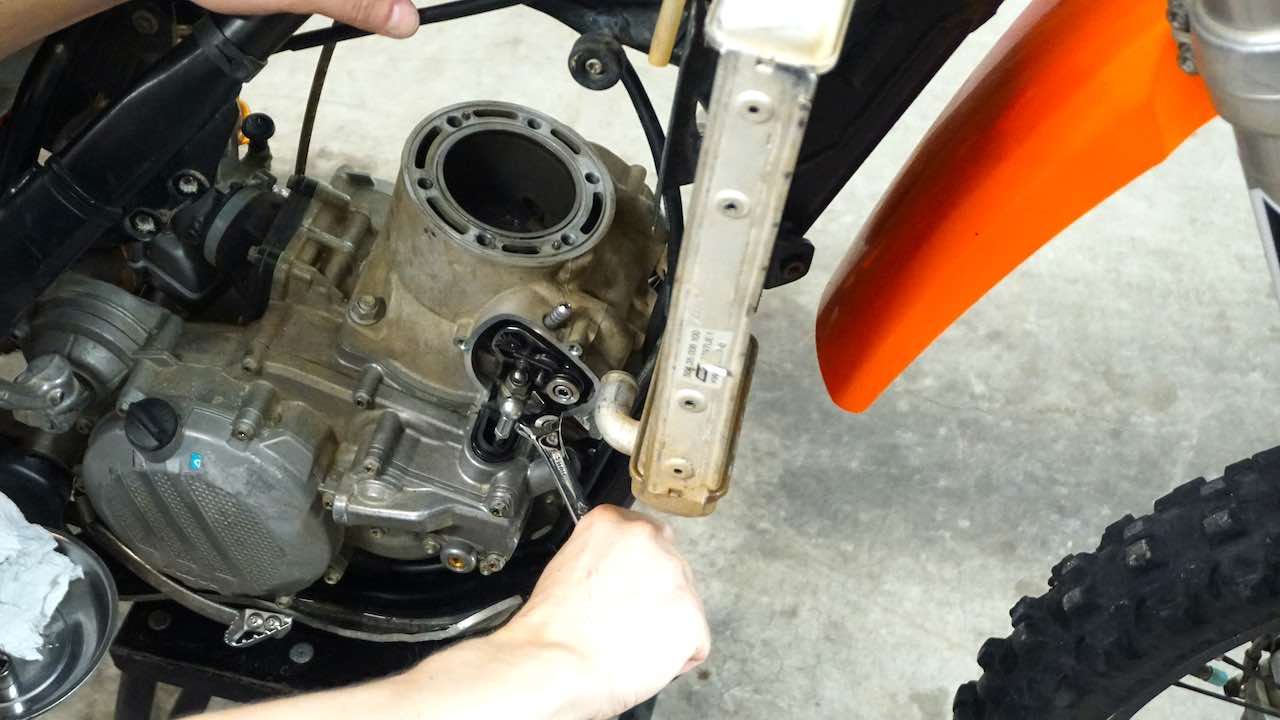 A hand holding a wrench and loosening a front cylinder base nut
