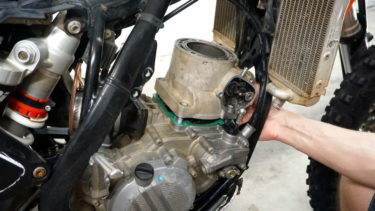 A hand lifting the cylinder out of the dirt bike motor