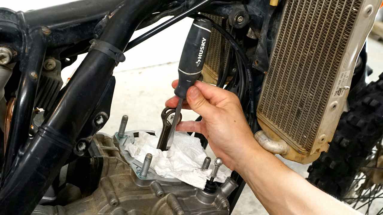 A hand holding a screwdriver next to the piston connecting rod in the direction of the stroke