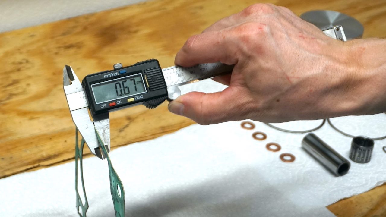 A hand holding a digital caliper and measuring the base gasket thickness