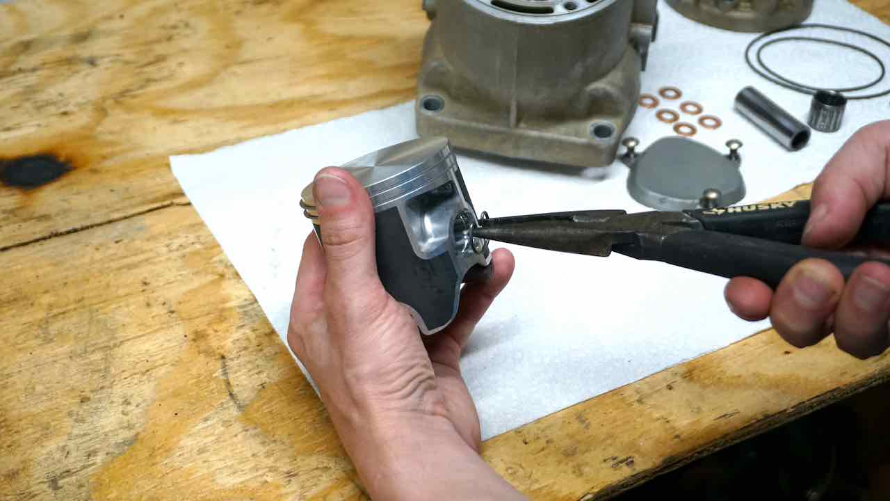 Hands holding a piston and inserting a piston circlip into place with pliers