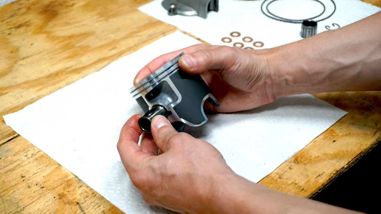 Hands holding a piston and sliding a wrist pin into place over a workbench