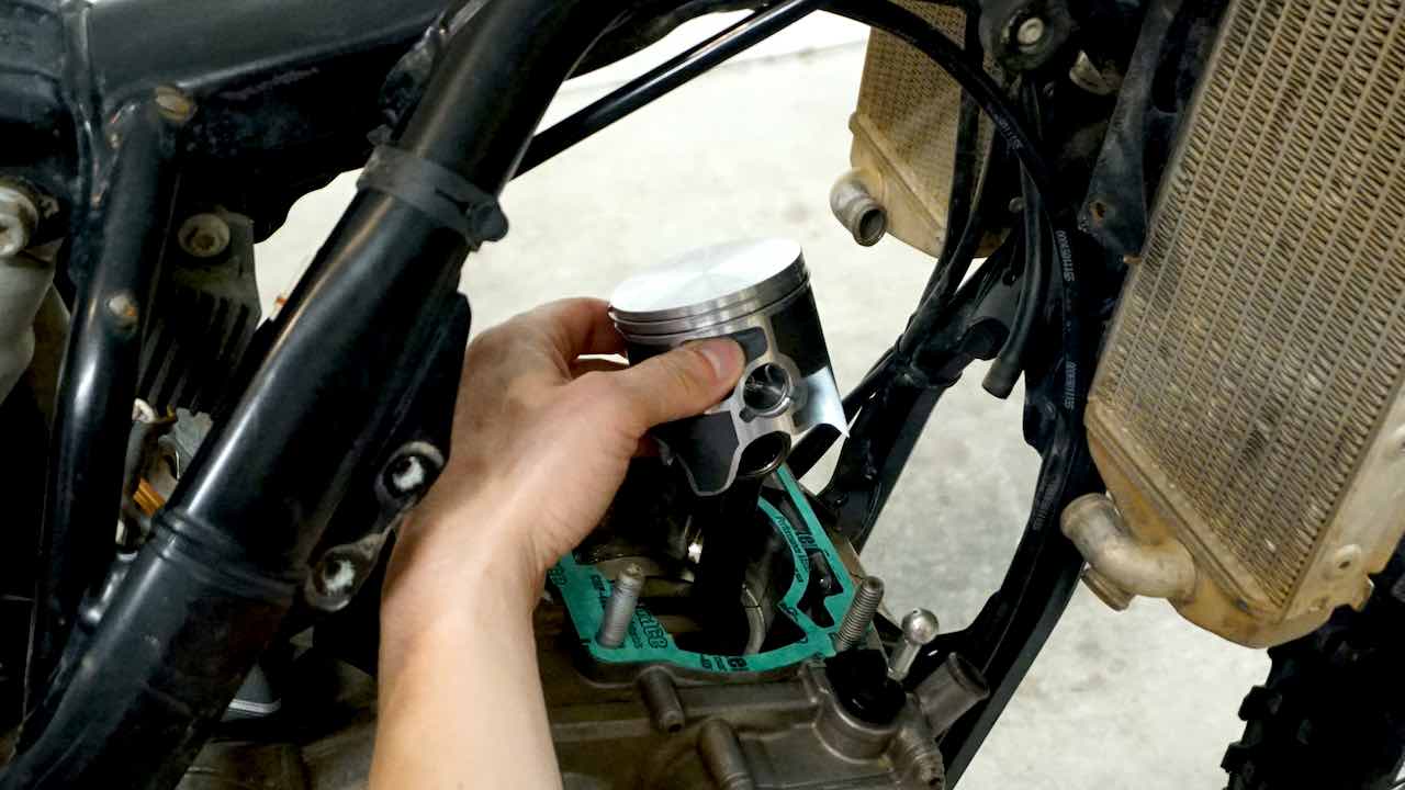 A hand holding a new piston and installing it on the connecting rod while performing a 2 stroke top end rebuild