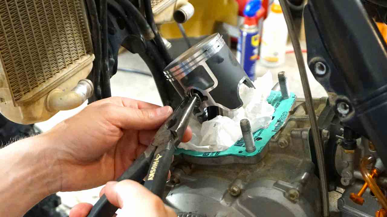 Hands holding pliers and inserting the new left side piston circlip into the dirt bike piston