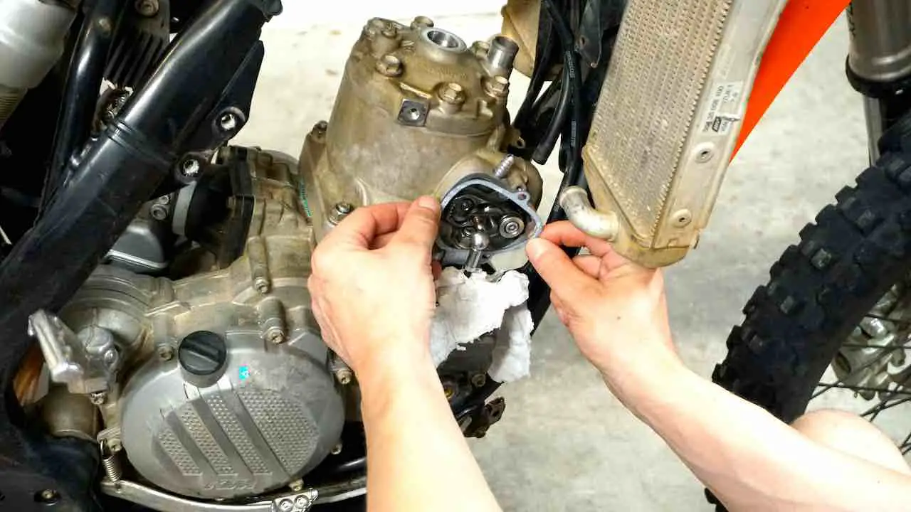 Hands holding a power valve cover gasket and inserting it in the dirt bike power valve