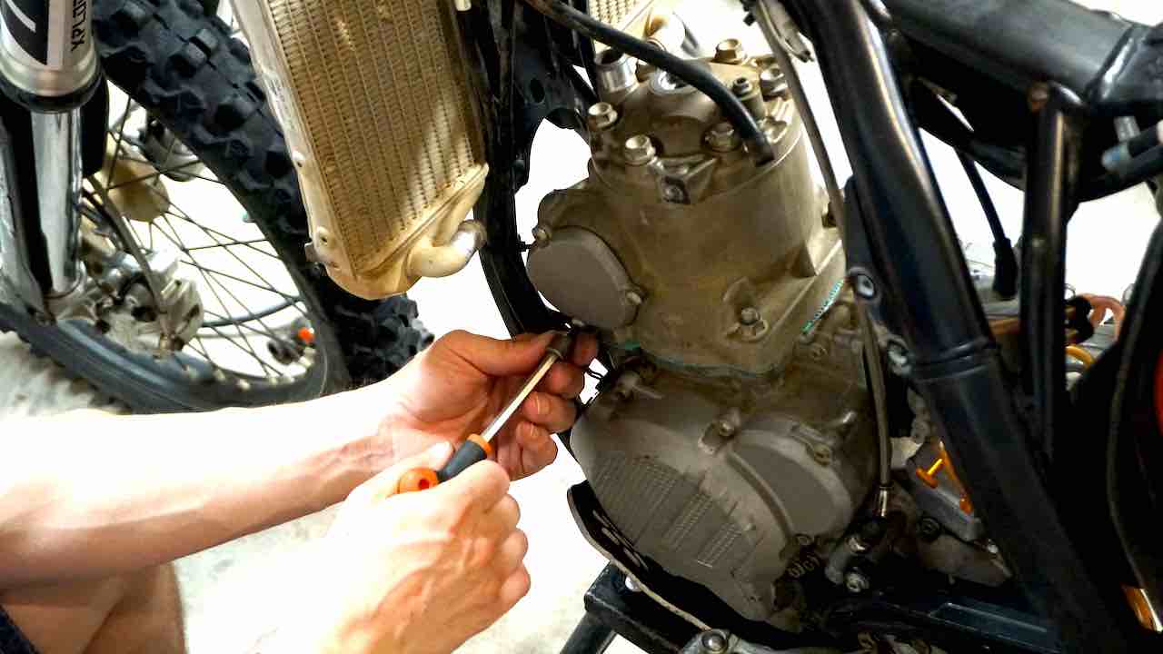 Hands holding a T-handle tool and tightening the power valve cover bolts during a 2 stroke top end rebuild