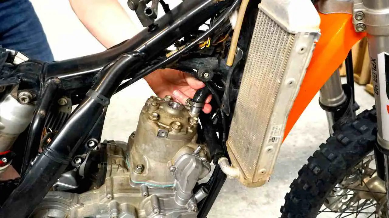 A hand holding a radiator hose and installing it on the top of the cylinder head
