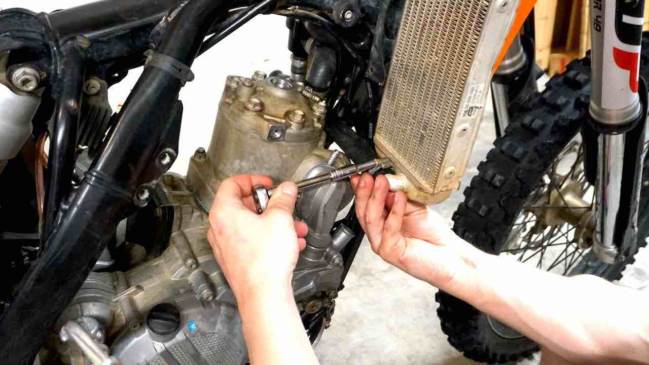 Hands holding a wrench and installing a connecting radiator hose on the dirt bike radiator