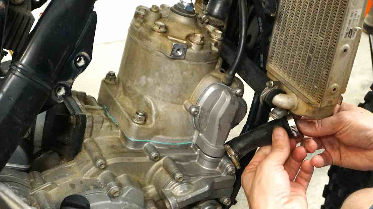 Hands holding a lower radiator hose and installing it in the dirt bike radiator