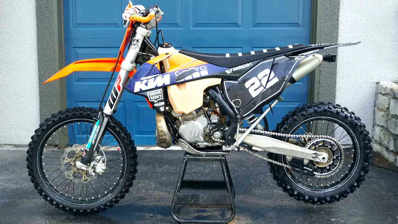 A freshly washed dirt bike standing on a center stand in front of a blue garage door