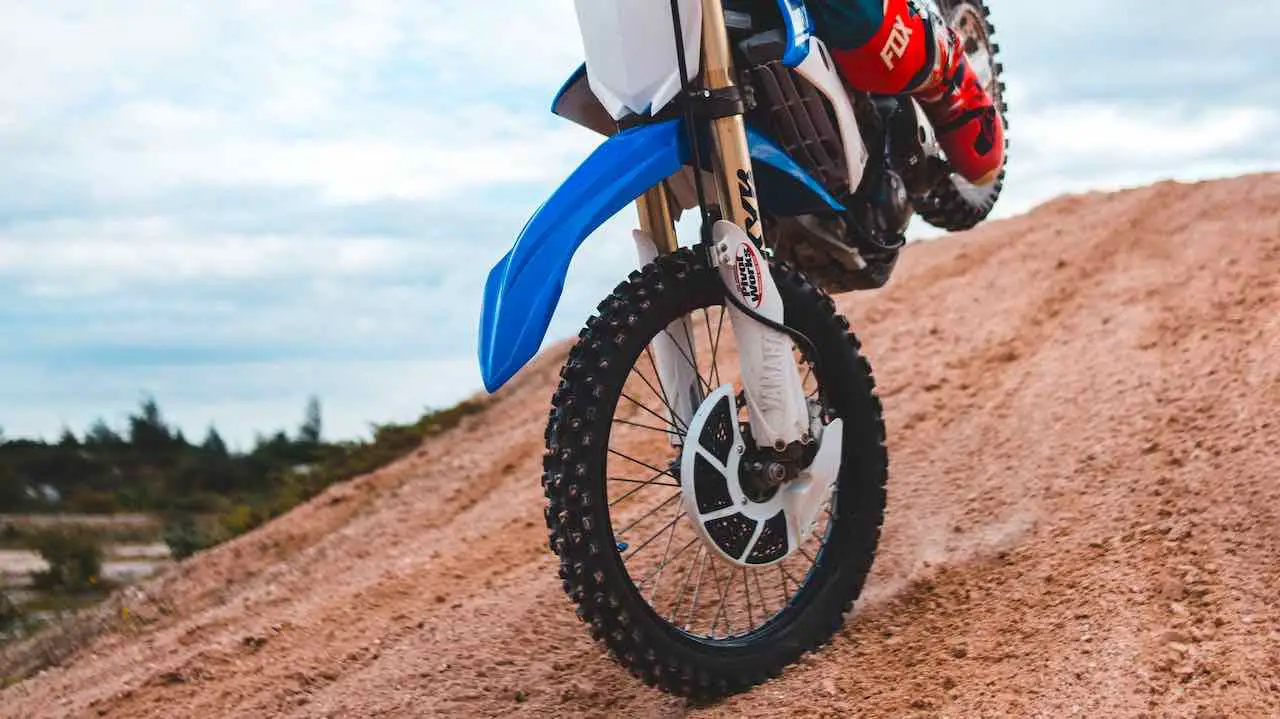 A front wheel of a dirt bike touching the ground while riding down a sandy hill
