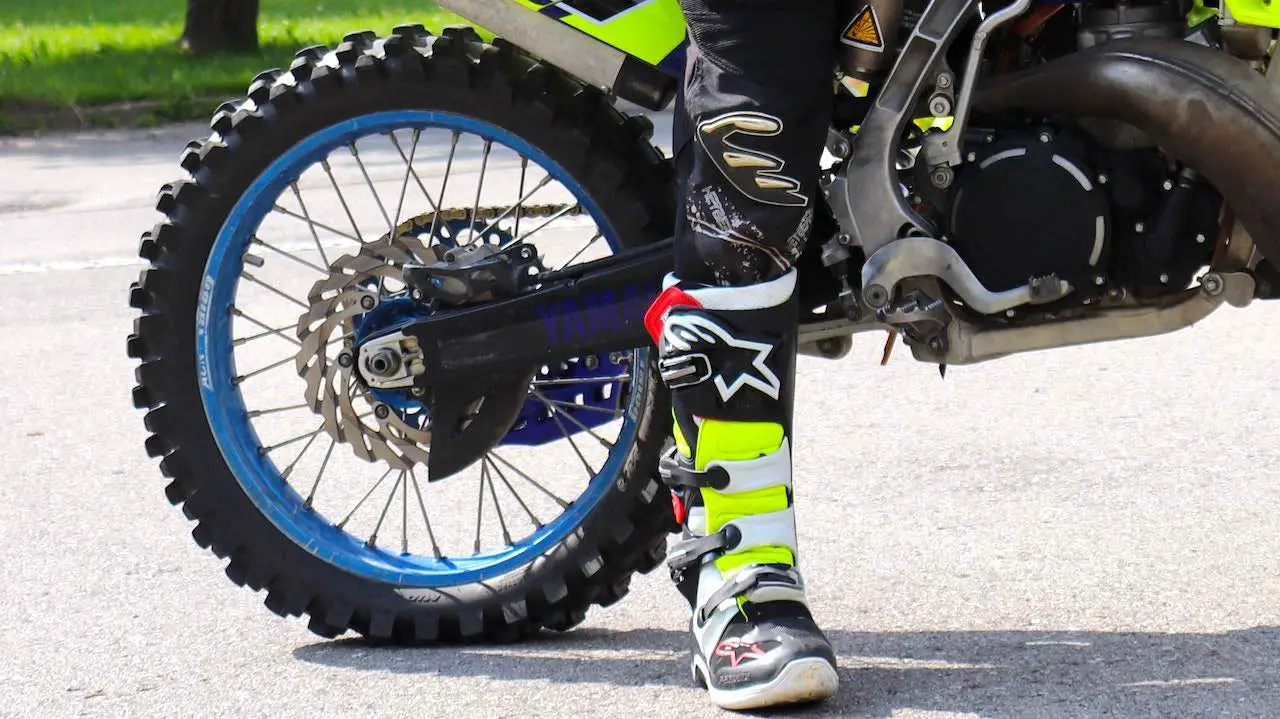 Dirt bike rider's right foot standing next to the rear wheel that is protected with a brake disc cover